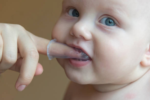 istock Mom brushes baby's teeth with a brush that fits on her finger 1063008788