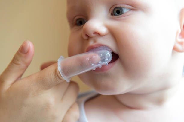 istock Mom brushes baby's teeth with a brush that fits on her finger 1063009324