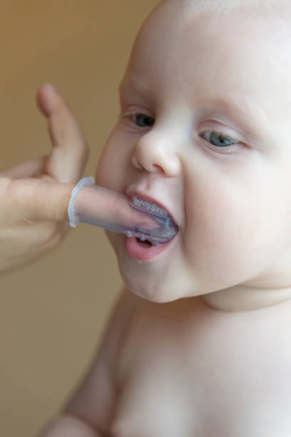istock Mom brushes baby's teeth with a brush that fits on her finger 1063009964