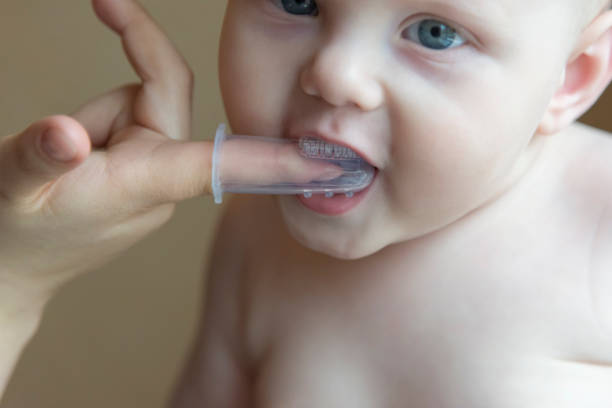 istock Mom brushes baby's teeth with a brush that fits on her finger 1063011018