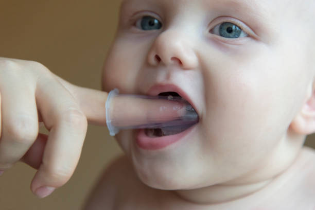 istock Mom brushes baby's teeth with a brush that fits on her finger 1063011276