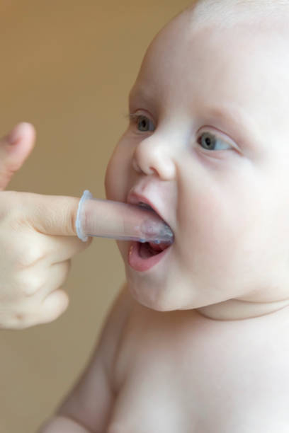 istock Mom brushes baby's teeth with a brush that fits on her finger 1063011454