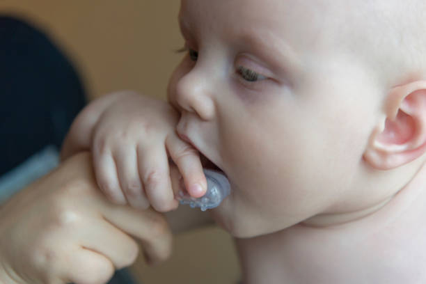 istock Mom brushes baby's teeth with a brush that fits on her finger 1063011554
