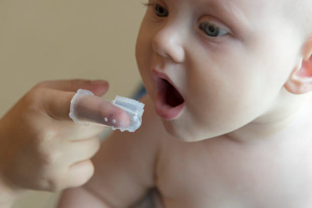Mom brushes baby's teeth with a brush that fits on her finger