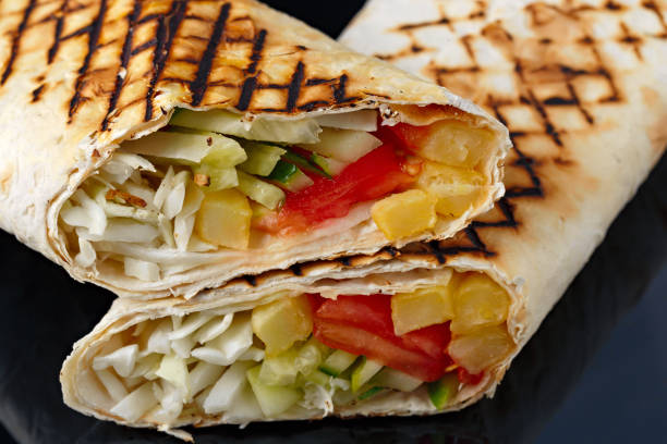 istock Shawarma in pita bread is cut and lies on a black reflective background. The Middle Eastern dish is prepared on the grill and served with sauce. 1063018014