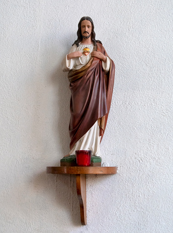 A figurine of Jesus Christ, indicating his heart, standing with a candle on a plinth attached to the wall of the parish church of St Nicholas in Wells-next-the-Sea, Norfolk, Eastern England.