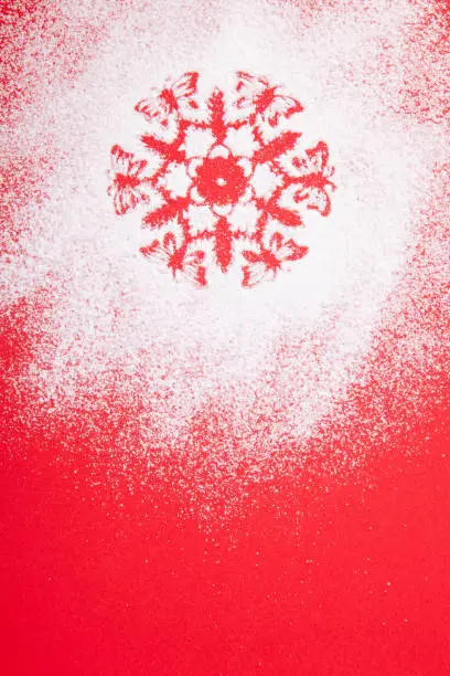 White, snow, stencil snowflake, sweet icing sugar on a red background, congratulations on Christmas holidays, a symbol of winter.