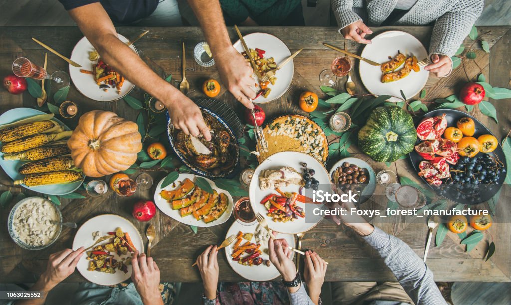 Flat-lay of friends feasting at Thanksgiving Day table with turkey Traditional Thanksgiving or Friendsgiving holiday celebration party. Flat-lay of friends or family feasting at Thanksgiving Day festive table with turkey, pumpkin pie, roasted seasonal vegetables and fruit, top view. Thanksgiving - Holiday Stock Photo