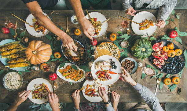 Flat-lay of friends feasting at Thanksgiving Day table with turkey Traditional Thanksgiving or Friendsgiving holiday celebration party. Flat-lay of friends or family feasting at Thanksgiving Day festive table with turkey, pumpkin pie, roasted seasonal vegetables and fruit, top view. dinner party stock pictures, royalty-free photos & images