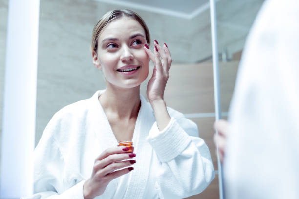istock Appealing woman wearing bathrobe putting some cream on her face 1063044512