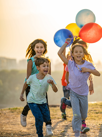 Beauty kids running at sunset with multi colored balloons
