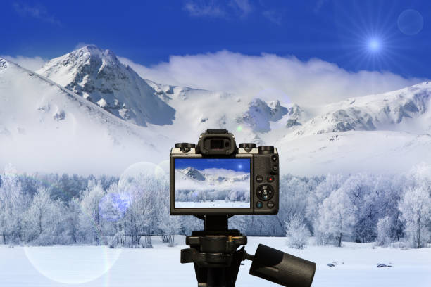Camera and winter landscape with a road, trees and mountains covered with a fresh layer of white snow and with a blue sky