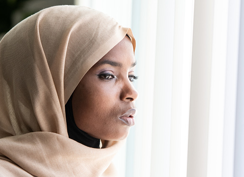 Concerned immigrant black muslim woman looking through a window