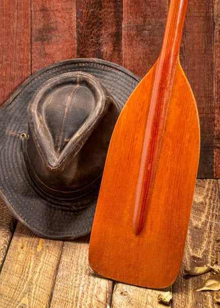 wooden blade of a canoe paddle with a weathered outback hat against rustic barn wood