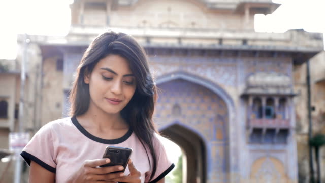 An attractive girl using smartphone or cellphone and walks on the busy town road