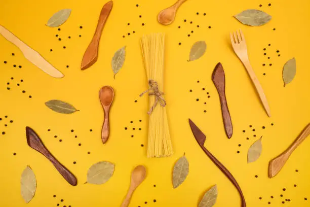 Handcrafted wooden utensils, pasta and spices. Flat lay composition on bright yellow background.