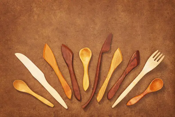 Handcrafted wooden utensils on brown leather background. Fork, spoons and knives.