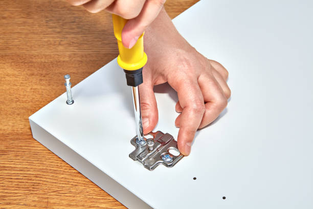handyman fixes furniture door hinges of white wooden table. - screwdriver screw tighten fastener imagens e fotografias de stock