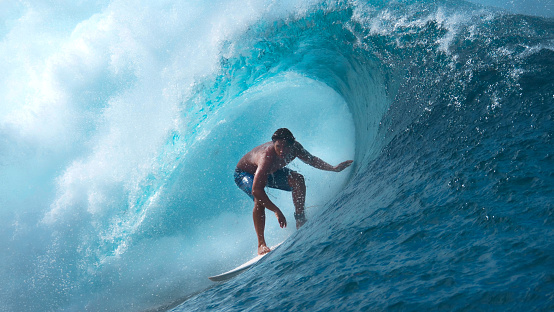 CLOSE UP Crystal clear water splashes over surfer riding an epic barrel wave in spectacular Tahiti. Extreme pro sportsman surfing a breathtaking emerald wave on a perfect sunny day in French Polynesia