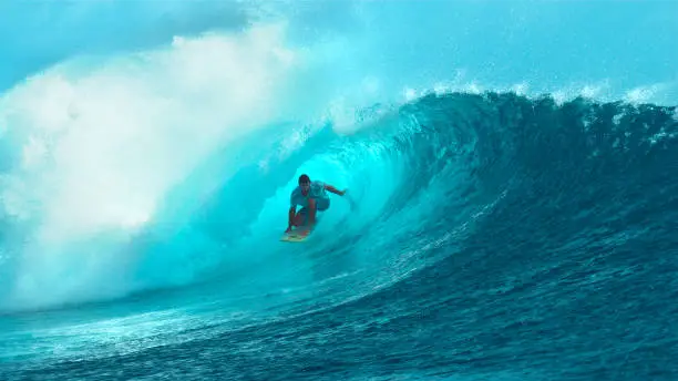 CLOSE UP: Fearless young surfboarder rides inside a spectacular barrel wave. Breathtaking shot of wild emerald wave curling and splashing over a pro male surfer having fun in sunny French Polynesia.