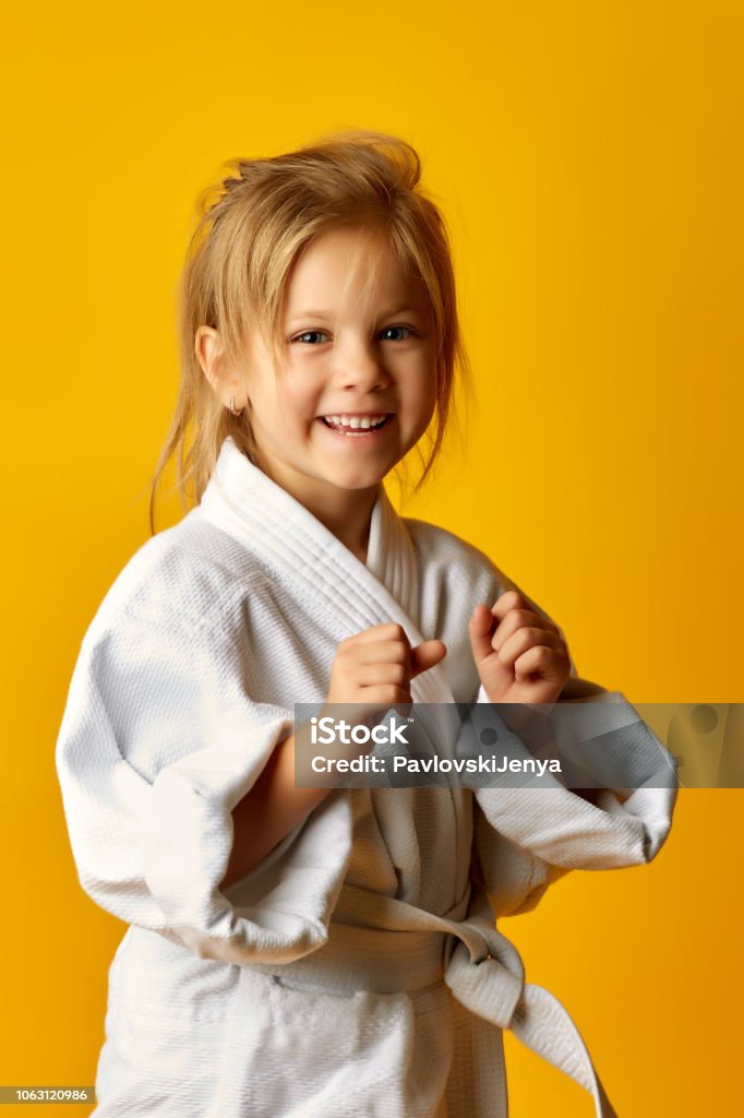 Girl on a yellow background with white belt is hitting right hand The karate girl on a yellow background with white belt is hitting right hand Child Stock Photo