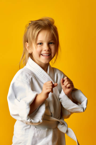 garota em um fundo amarelo com faixa branca é bater a mão direita - karate child judo belt - fotografias e filmes do acervo