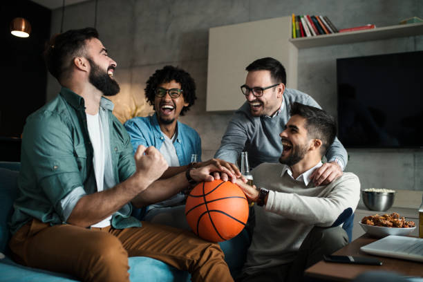 un gruppo di giovani uomini d'affari guardare una partita di basket in tv dopo il lavoro - colleague looking at camera indoors lifestyles foto e immagini stock