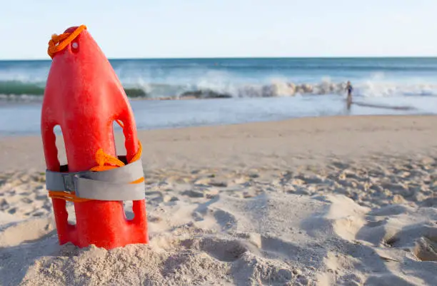 Orange rescue buoy planted on sand beach. Little boy close to the waves at the bottom. Hazardous scene