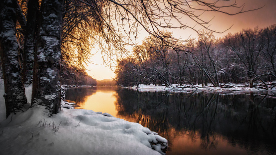 The beauty of winter. A soft golden sunset warms the sky over Michigan's Grand River. Tranquil natural background with copy space. Vintage look.