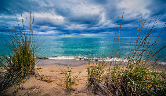 Peaceful waves lap onto a sandy beach as heavy storm clouds roll in over a calm Lake Michigan on this relaxing evening at Kirk Park. Tranquil shoreline seascape background with copy space.