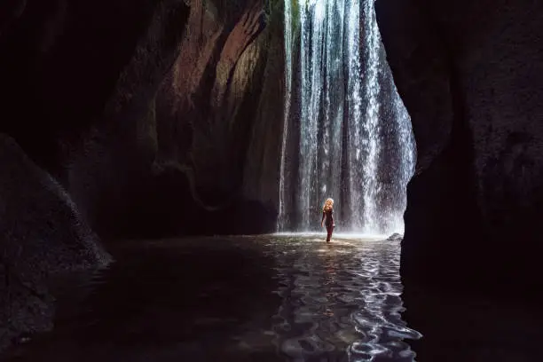 Photo of Woman stand under cave waterfall