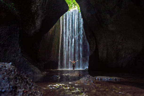 istock Woman stand under cave waterfall 1063159790
