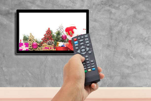 istock christmas decoration with hand holding remote control at television screen with concrete wall for background. 1063201238