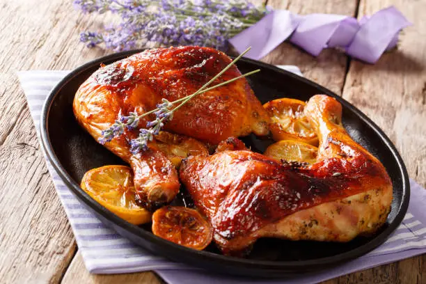 Delicious food: grilled glazed chicken legs with lavender honey and lemon close-up on a plate on the table. horizontal