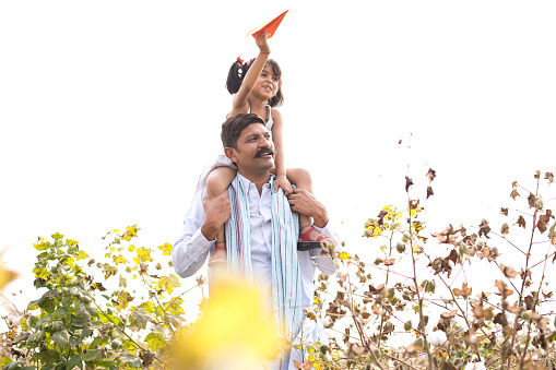 Girl throwing paper airplane while sitting on father's shoulder in agriculture field