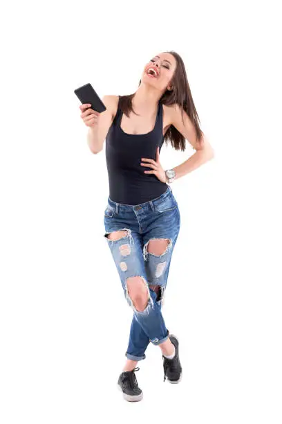 Expressive laughing hard young beautiful woman with mobile phone bending head backwards. Full body isolated on white background.