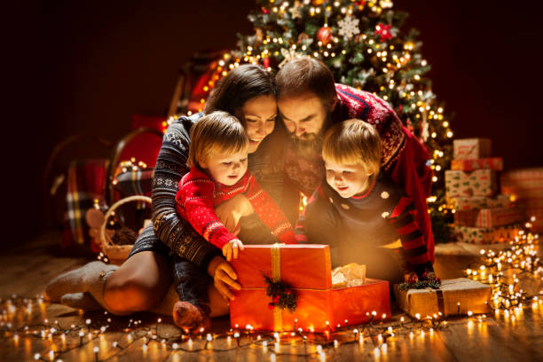 weihnachten familie öffnen beleuchtung präsent geschenk-box unter weihnachtsbaum, glückliche mutter-vater-kinder - weihnachten familie stock-fotos und bilder