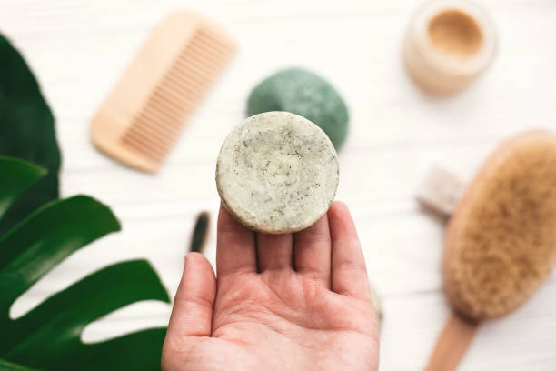 main tenant la barre de shampooing solide naturel sur fond de brosse de bambou, déodorant, éponge sur bois blanc avec feuilles de monstera vert. zéro déchet. produits de choix en plastique eco gratuit - état solide photos et images de collection