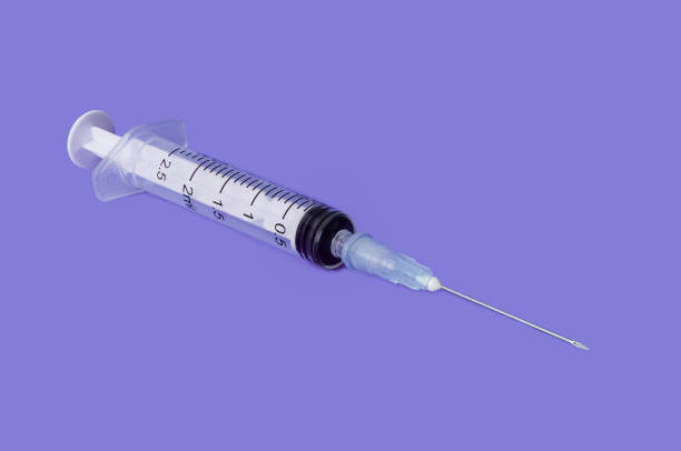 istock Transparent disposable syringe with needle on lilac background. 1063244562