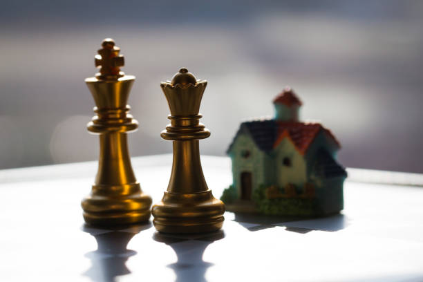 Vibrant blue chess pieces, including a king and queen, are prominently displayed on a reflective glass chessboard, with silhouettes of other pieces creating a dramatic interplay of light and shadow in the background