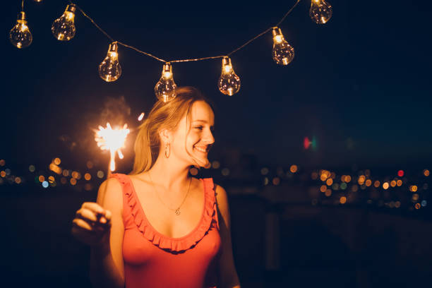 Young woman posing with string light and sparkler on a rooftop
