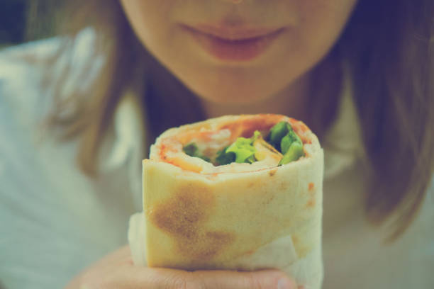 Woman holding sandwich wrap with ham, cheese and lettuce.