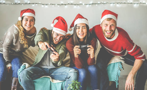 gruppo di amici felici che si divertono con la console per videogiochi nel periodo natalizio - giovani millennial che giocano e ridono durante le vacanze invernali con luce vintage sullo sfondo - concentrati sul viso dell'uomo giusto - friendship video game young adult party foto e immagini stock