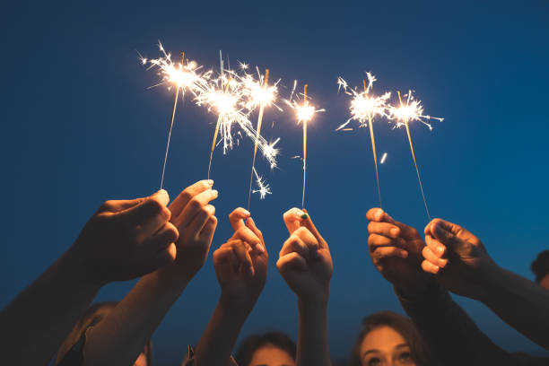 Friends celebrating new years eve with firework Close up of young people hands holding sparklers against sky. Friends celebrating new years eve with fireworks. sparkler stock pictures, royalty-free photos & images