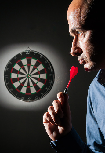 Closeup view of a dart player on a black background concentrating on the dartboard