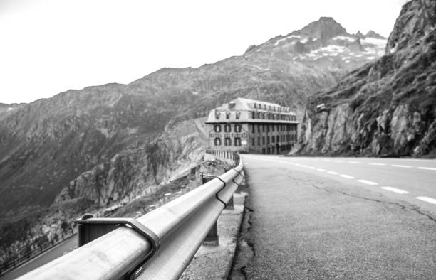 Low perspective, black and white image of a mountain road with building in the Swiss Alps.
