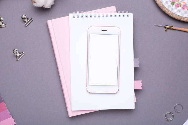 istock Mobile phone with white notepad , pink notebook and embroidery on grey background 1063290152