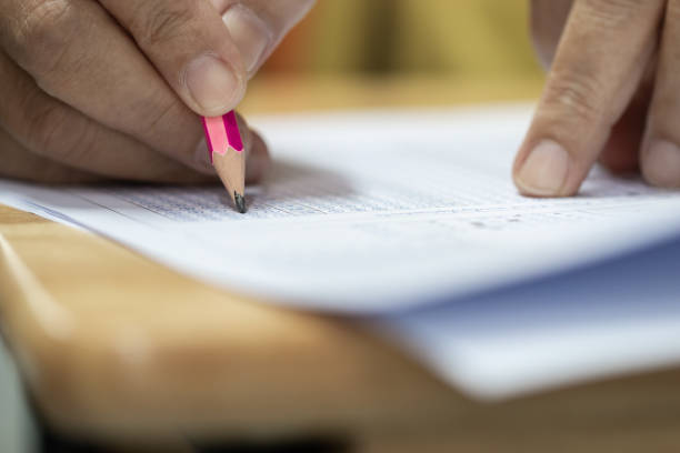 istock Education test concept : Hands student holding pen for testing exams writing answer sheet or exercise for taking fill in exam carbon paper computer on wood table at classroom in high school 1063294772