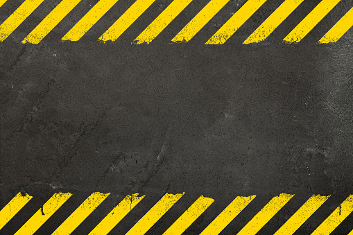Dark grey concrete weathered wall background with yellow painted grunge hazard sign stripes and copy space