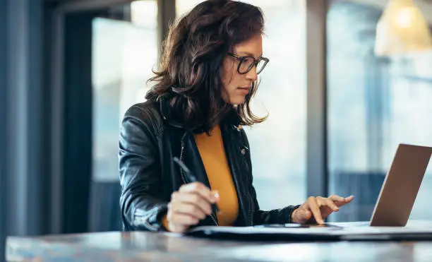 Photo of Businesswoman making notes looking at a laptop